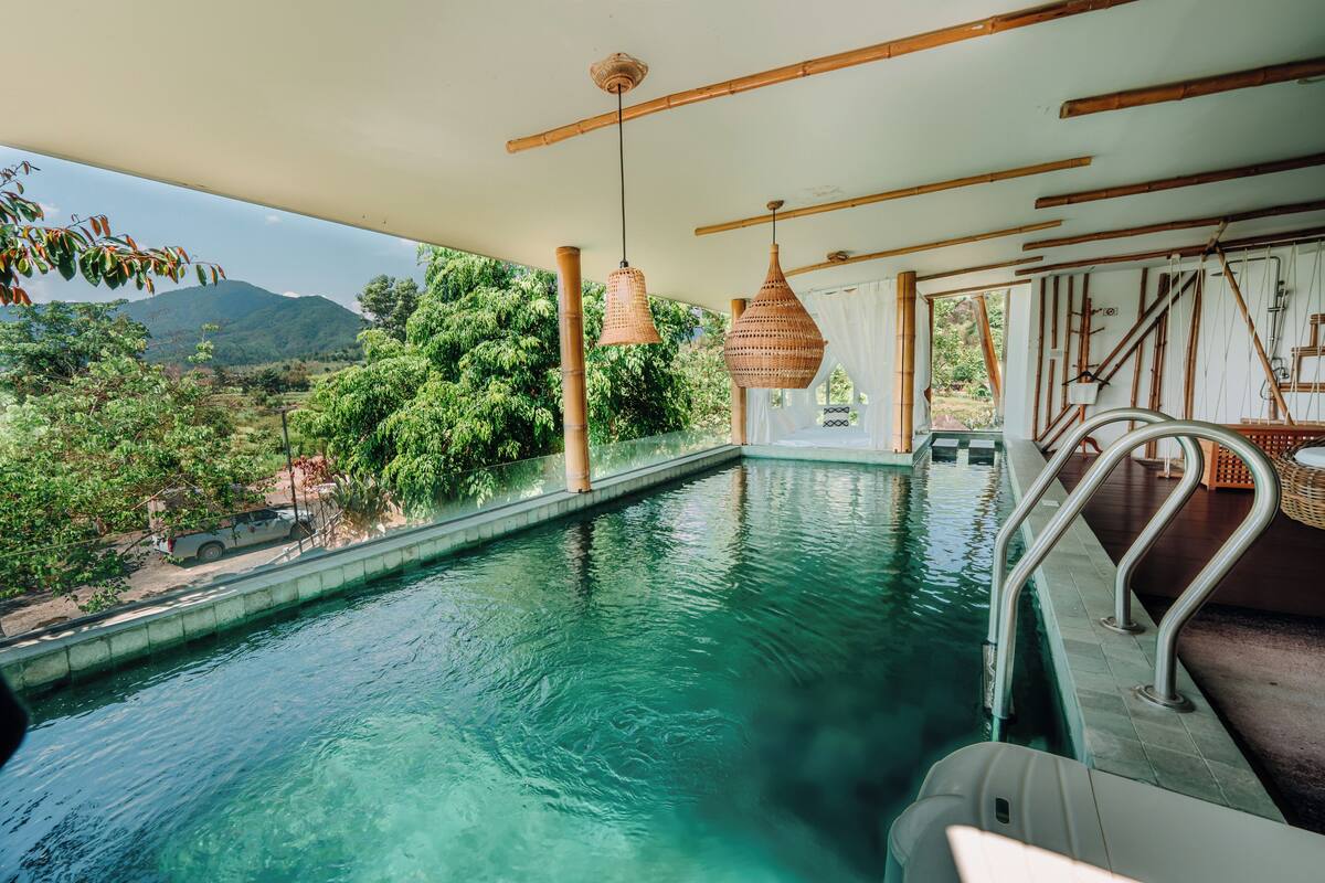 A pool with a view of a mountain and trees, bamboo beams, and hanging wicker lamps.
