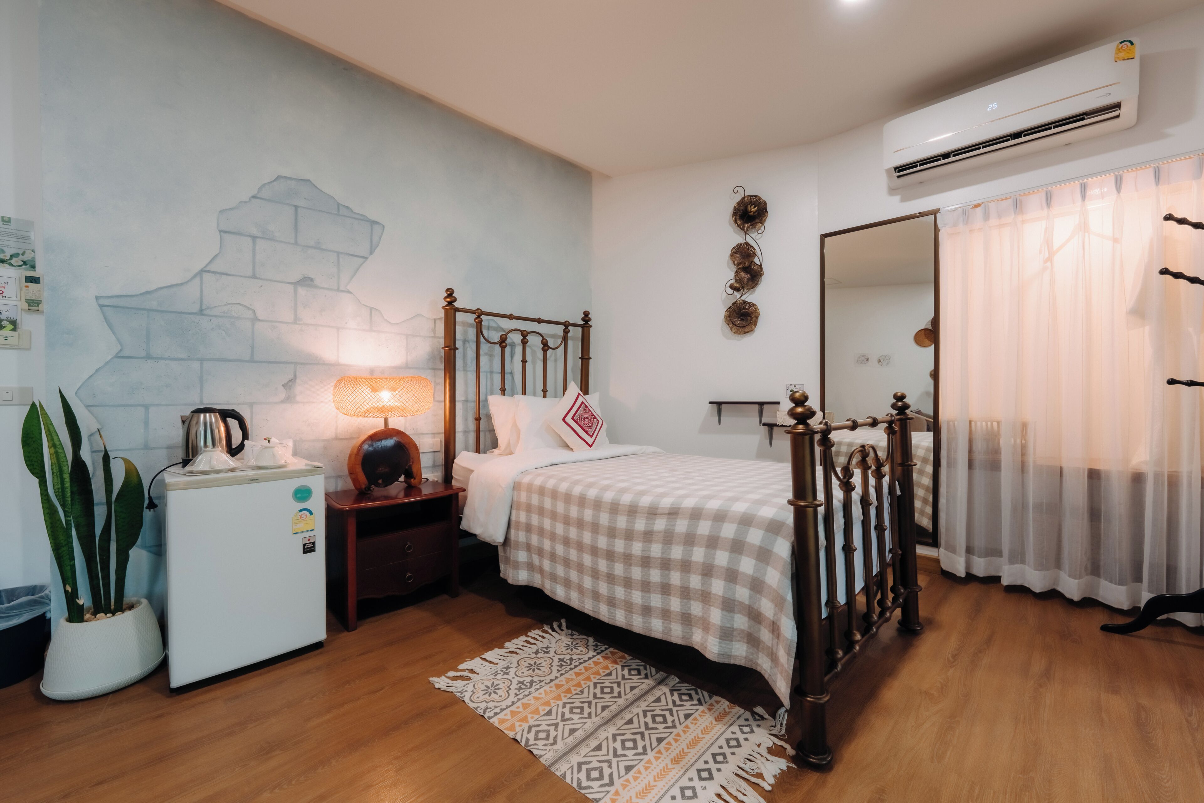A bedroom with a bed, bedside table, lamp, air conditioning unit, and a wall-mounted mirror.