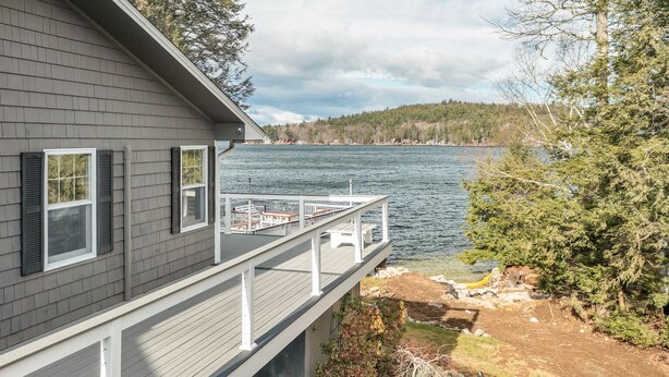 Ett hus med en veranda som vetter ut mot en sjö, omgivet av träd.