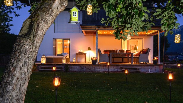 A modern house with a covered outdoor seating area, a visible window, and a tree in the foreground.