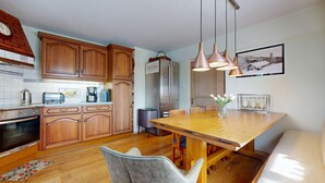 A modern kitchen with wooden cabinets, a stainless steel refrigerator, a coffee maker, and a dining table with chairs.