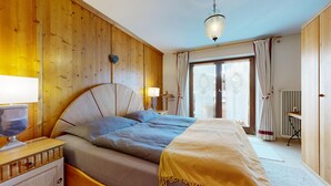 A bedroom with a bed, bedside lamps, a wooden headboard, a hanging heart decoration, and a window with curtains.