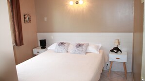 Een keurig opgemaakt bed met bloemenkussens, een bedlampje en een nachtkastje met lamp.