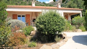 Een huis in mediterrane stijl met een pannendak, houten luiken en een stenen pad dat naar de ingang leidt.