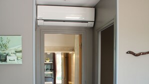 Een gang met in de achtergrond een badkamer, een witte airconditioning en een deur naar een andere kamer.