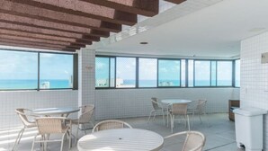 Un espace intérieur moderne, doté de grandes fenêtres, de meubles en osier et offrant une vue sur l’océan.