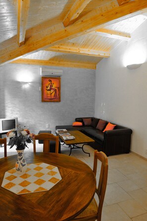 Un comedor con una mesa y sillas de madera, un cuadro en la pared y un sofá de cuero negro con cojines naranjas.