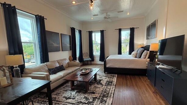 A modern bedroom with a bed, sofa, TV, and a dining area with a table and chairs. - In the heart of downtown Apalach w/ restaurants, shops & waterfront within steps (Apalachicola)