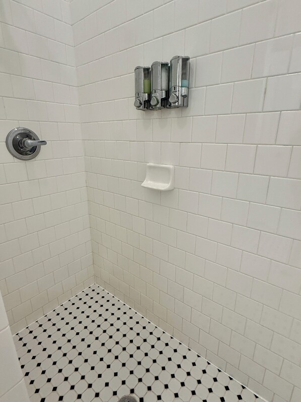 A shower with white tiles and a black and white patterned floor.