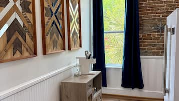 Una cocina con piso de madera, pared de ladrillo, ventana con cortinas y un refrigerador.