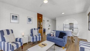 Un salon moderne avec des canapés bleus et blancs à rayures, une table basse et une cuisine visible à travers une arche.