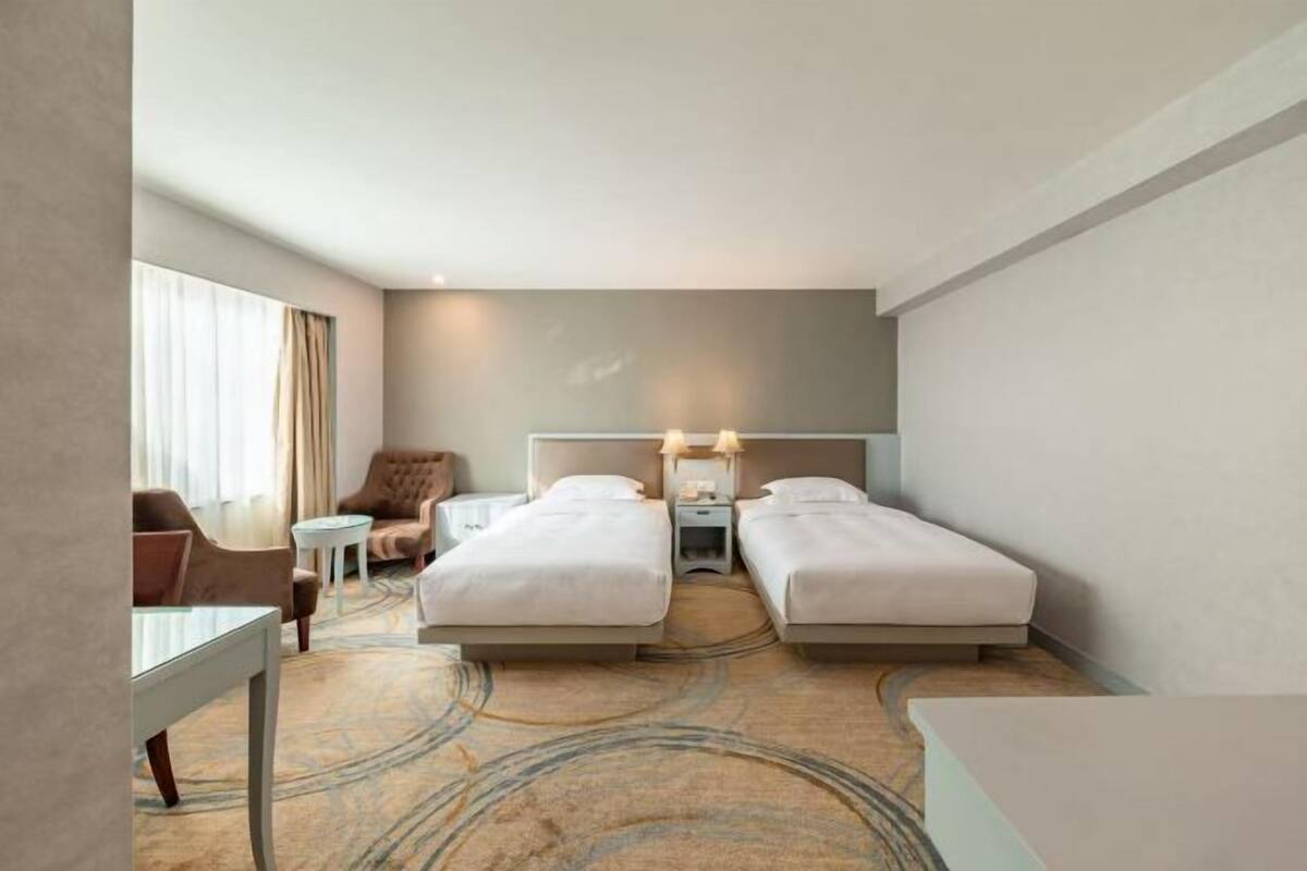 A hotel room with two beds, a desk, a chair, and a small table.