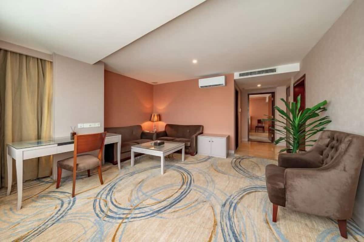A hotel room with a sofa, a desk, a coffee table, and a potted plant.