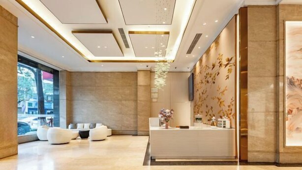 A modern reception area with a white reception desk, comfortable seating, and a decorative wall with a nature theme. - Dron Hotel (Dongguan)