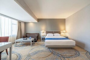 A hotel room with a bed, a desk, a chair, and a nightstand with a lamp. - Dron Hotel (Dongguan)