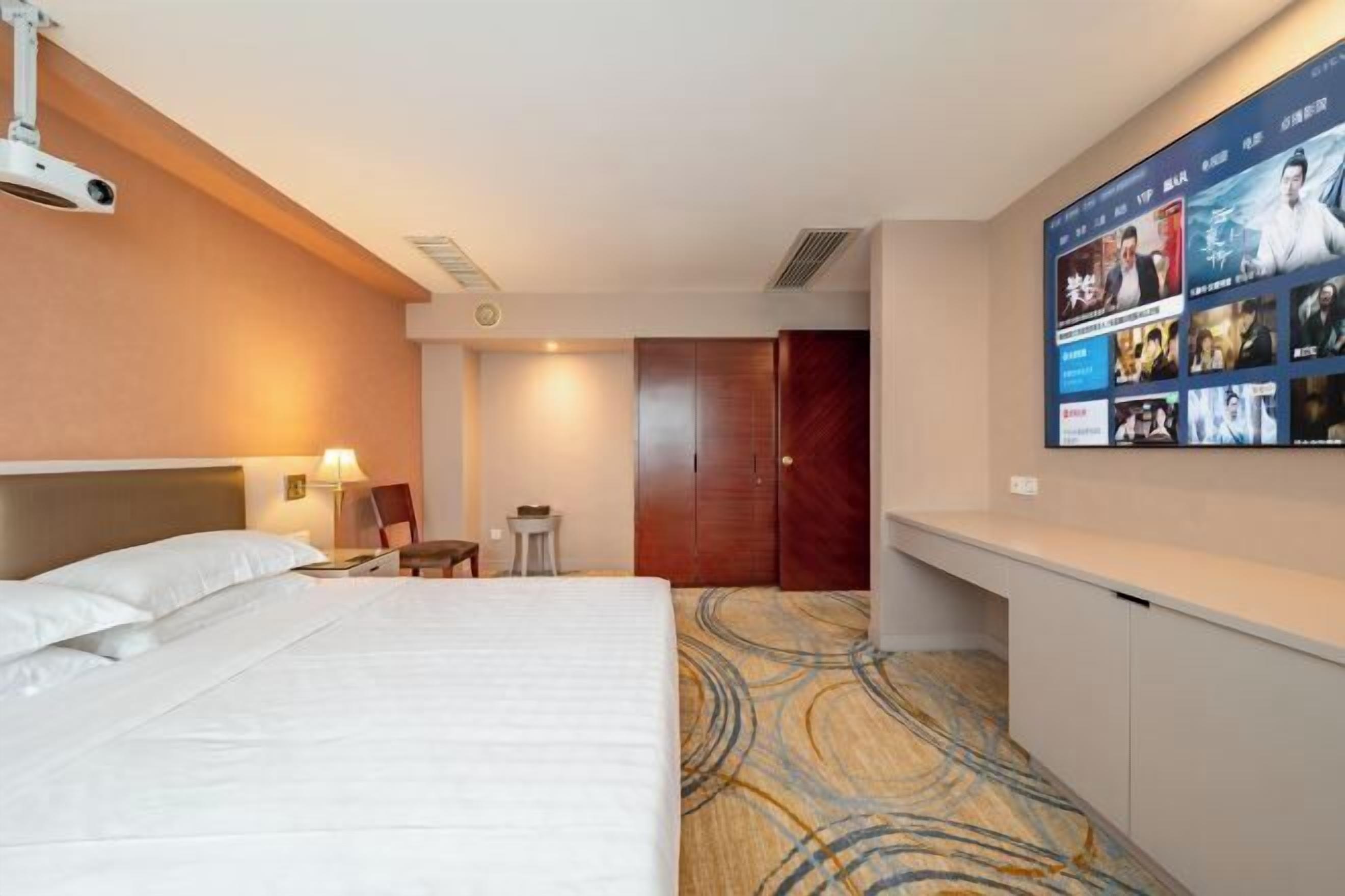 Une chambre d’hôtel avec un grand lit, un bureau, un téléviseur fixé au mur et un sol recouvert de moquette.