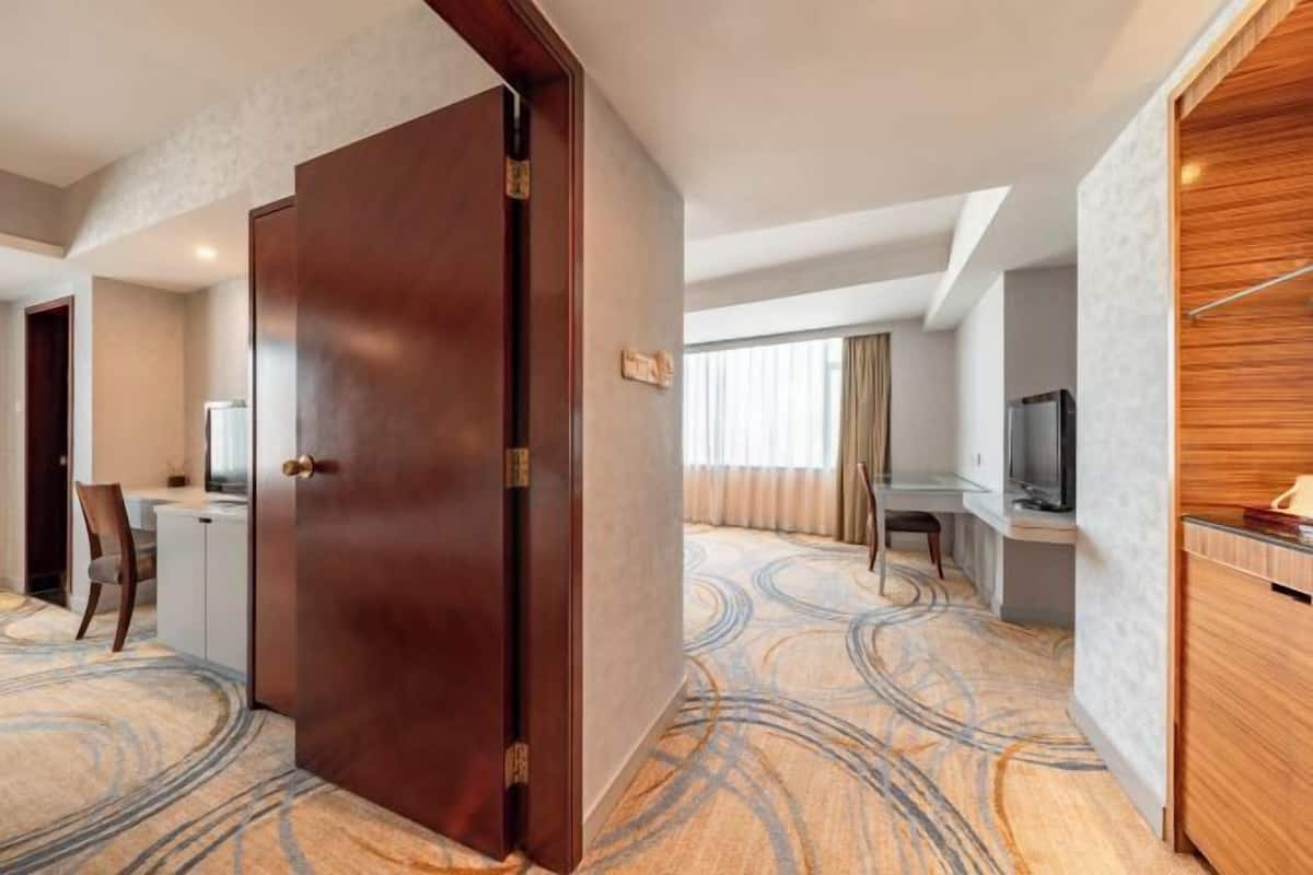 A hotel room with a wooden door, a desk with a chair, a television, and a patterned carpet.