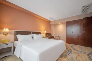 Ein Hotelzimmer mit einem großen Bett, zwei Nachttischlampen, einem Nachttisch, einem Sessel, einem Kleiderschrank und einem Teppich mit einem Rundmuster.
