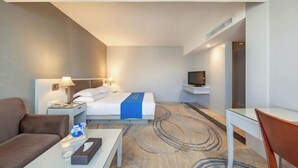 A hotel room with a bed, a desk, a television, a sofa, and a nightstand with a lamp. - Dron Hotel (Dongguan)