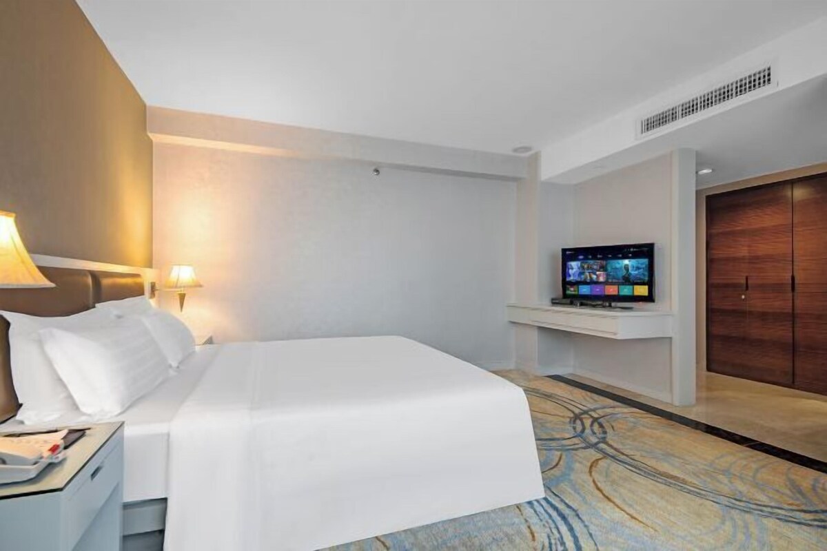 Ein Hotelzimmer mit Bett, Fernseher auf einem Tisch, Nachttisch und Kleiderschrank.