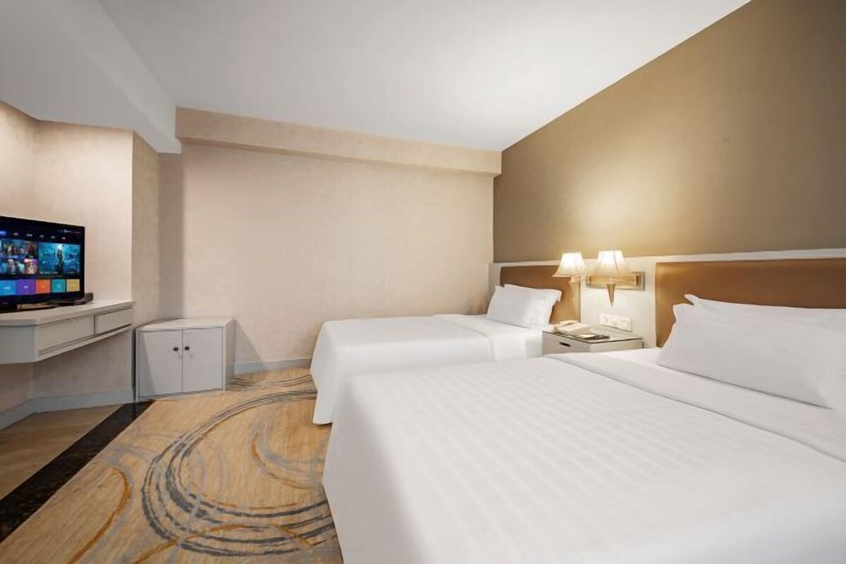 Ein Hotelzimmer mit zwei Betten, einem Fernseher, einem Schreibtisch und einer Lampe.