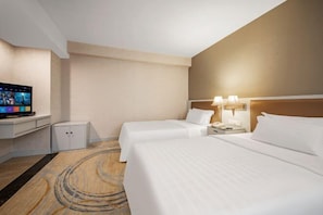 Ein Hotelzimmer mit zwei Betten, einem Fernseher, einem Schreibtisch und einer Lampe.