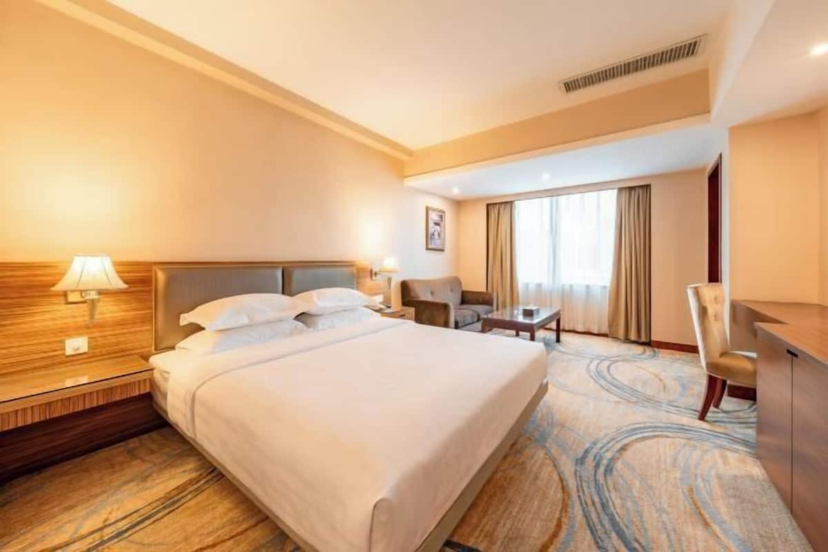 A hotel room with a large bed, a desk, a chair, and a window with curtains.