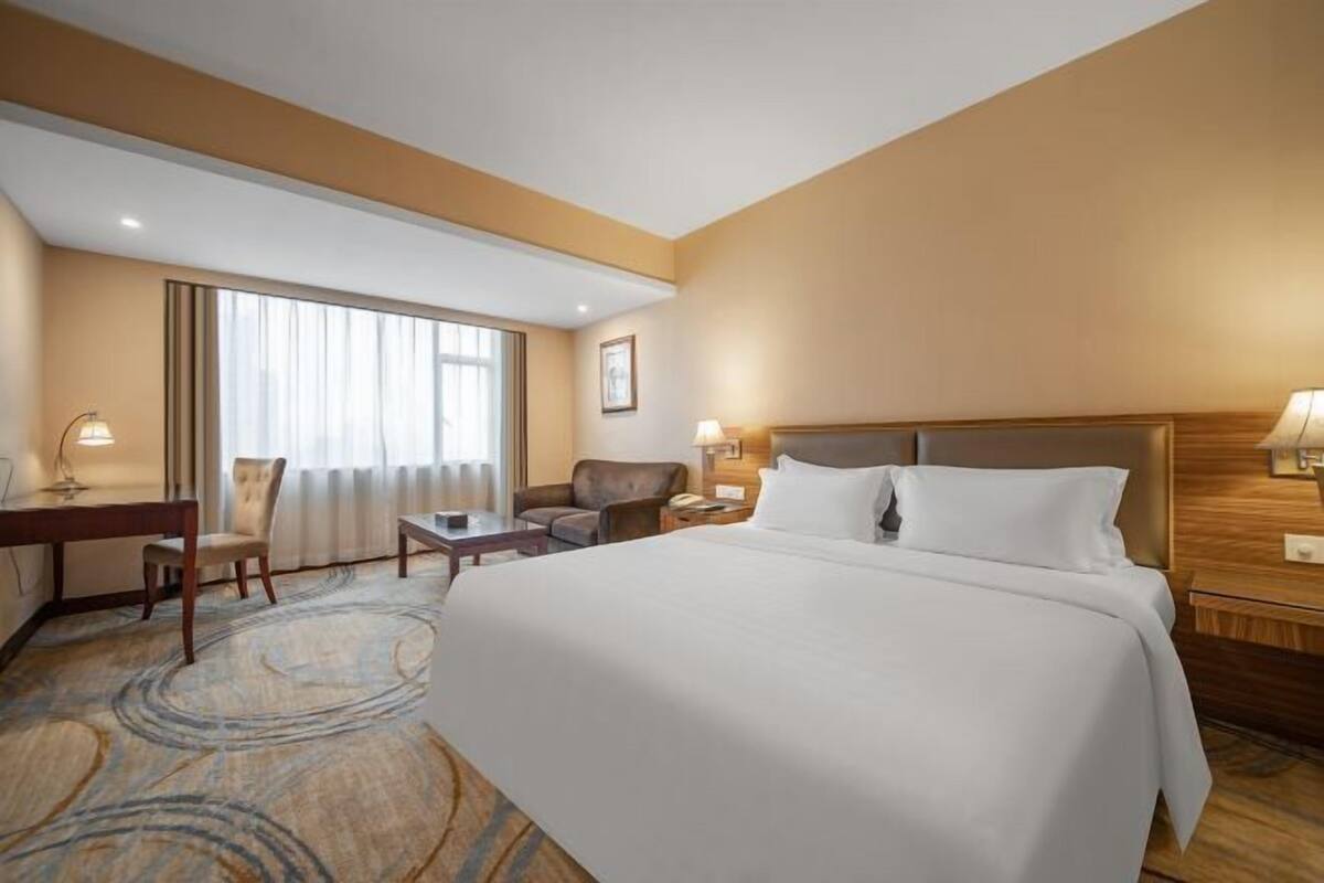 A hotel room with a large bed, a desk, a chair, and a window with curtains.