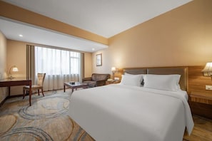 Ein Hotelzimmer mit einem großen Bett, einem Schreibtisch, einem Stuhl und einem fenster mit Vorhängen.