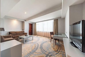 A modern hotel room with a sofa, a coffee table, a TV, and a large window with curtains.