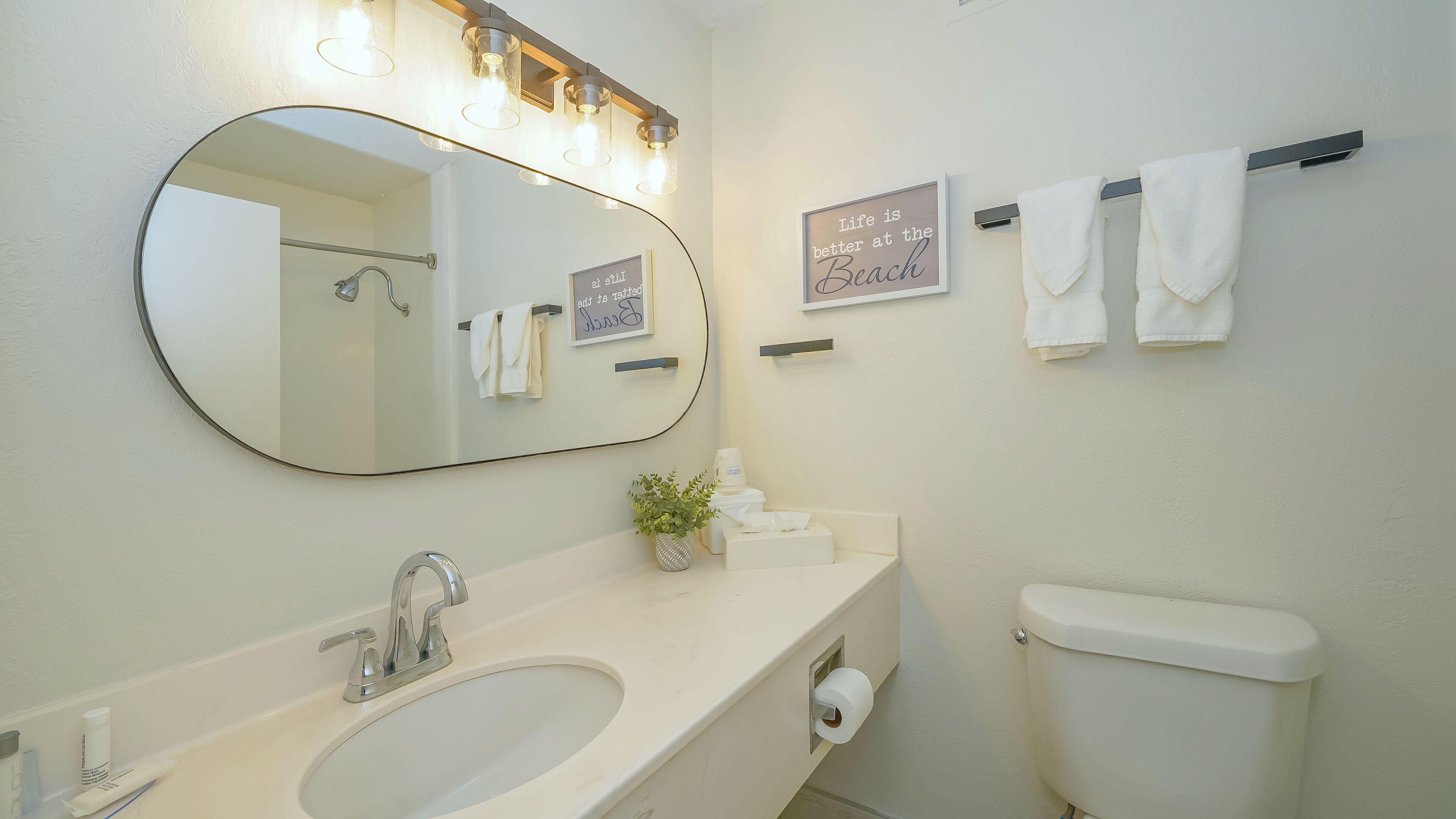 A bathroom with a sink, mirror, towel rack, toilet, and a framed inspirational quote on the wall.