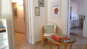 Een kamer met een rieten stoel, een glazen tafel met een boek en een boekenplank.