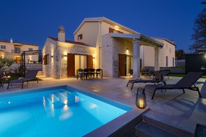Une maison moderne dotée d’une piscine, d’un espace salon extérieur et d’une terrasse bien éclairée.