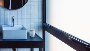 Un baño con un lavamanos blanco, un espejo redondo y una ventana con marco negro.
