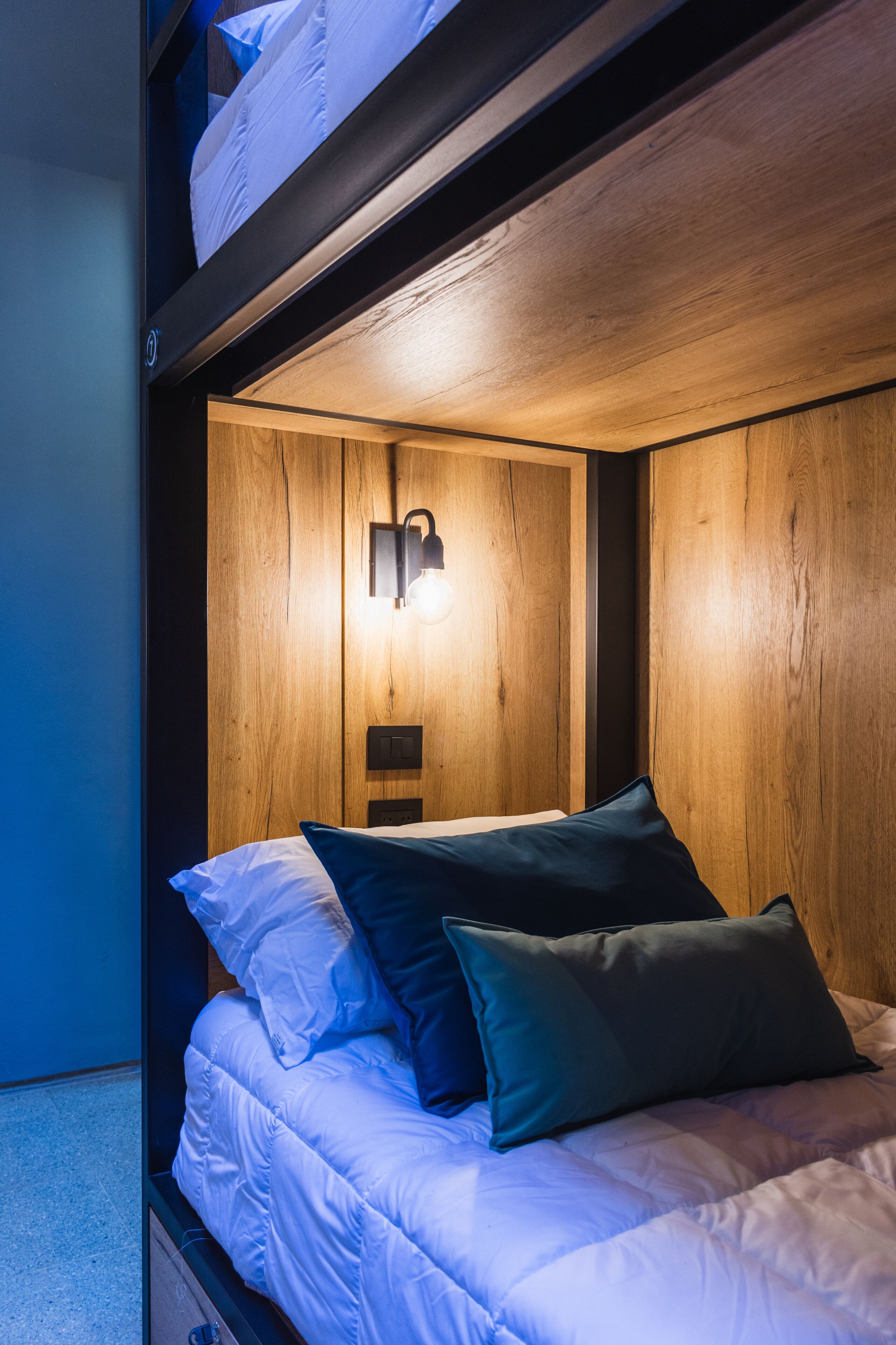 Un letto a castello con una testiera in legno, un lampadario fissato al muro e un singolo letto con cuscini.