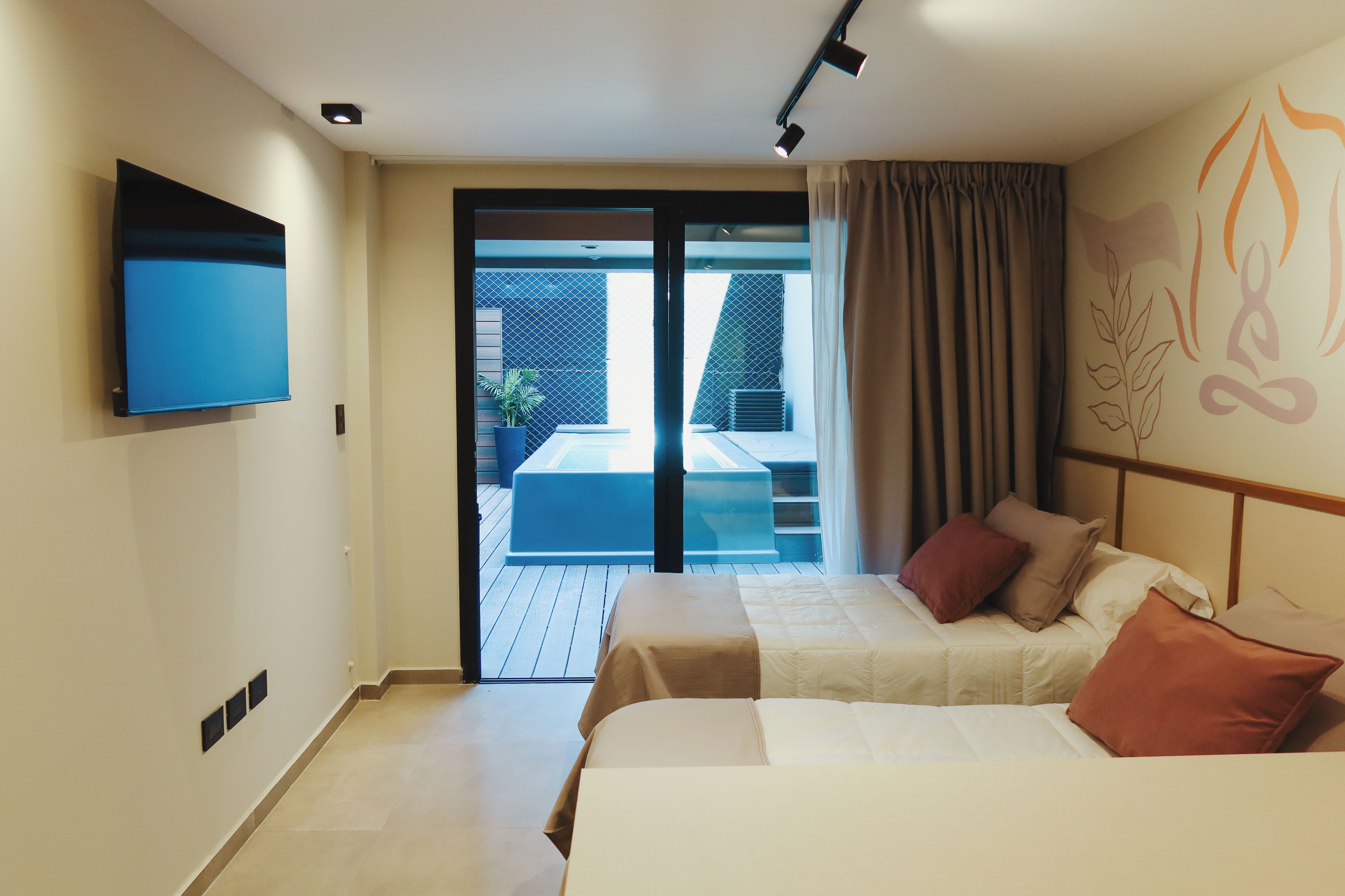 Habitación de hotel con cama, televisor de pantalla plana, puerta de vidrio corrediza que da a un espacio al aire libre y lámpara de techo.