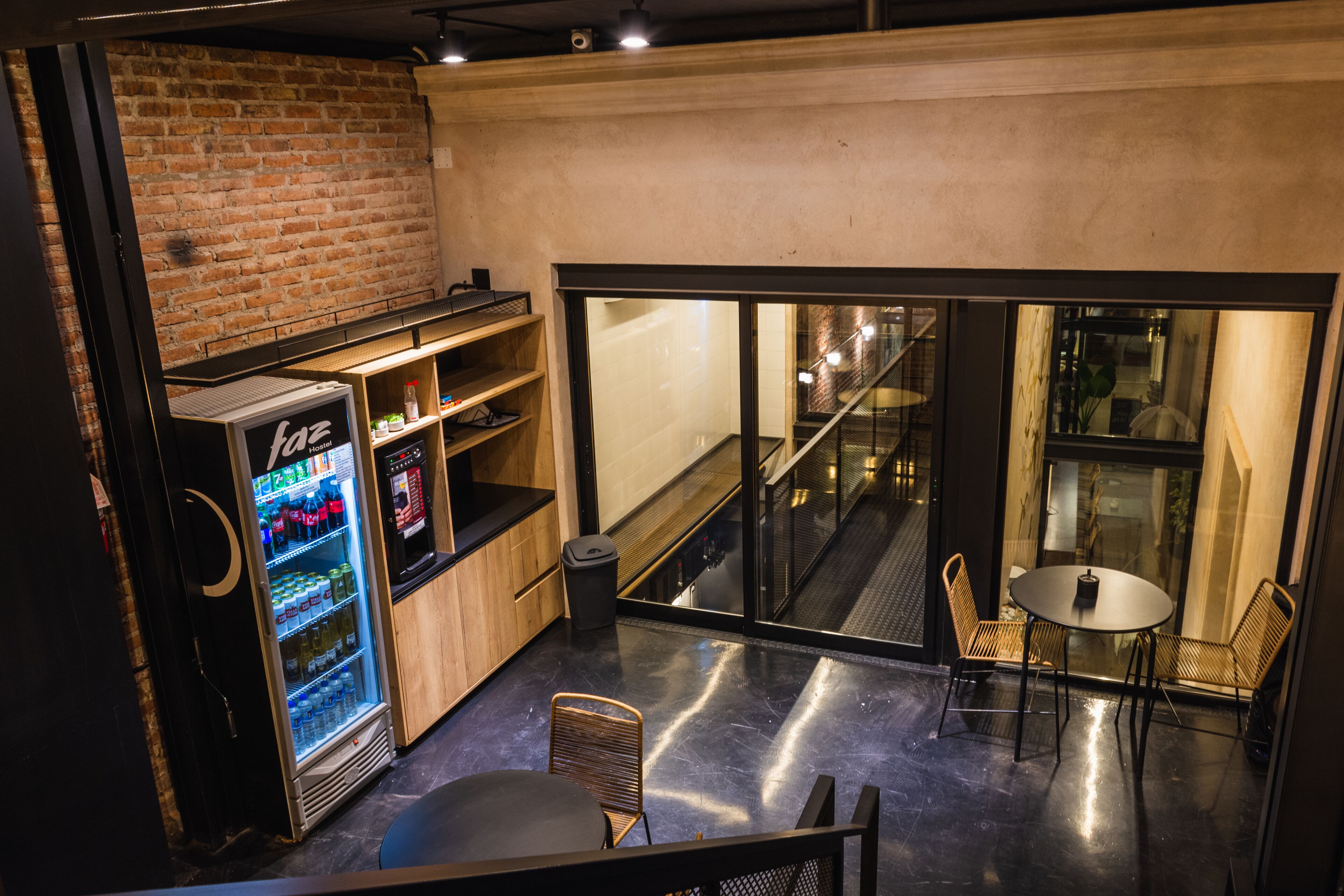A modern interior with a brick wall, a vending machine, a small table with chairs, and a view of a staircase.