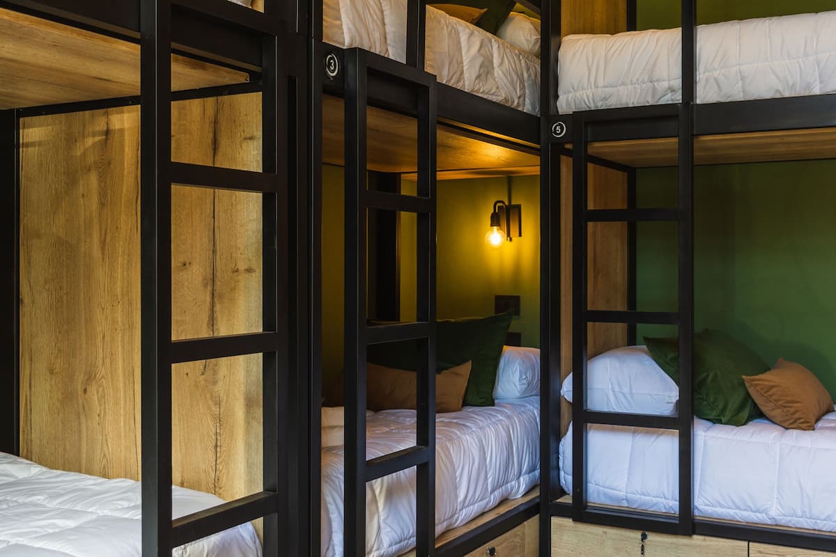 A bunk bed room with wooden frames, white bedding, and a green wall.