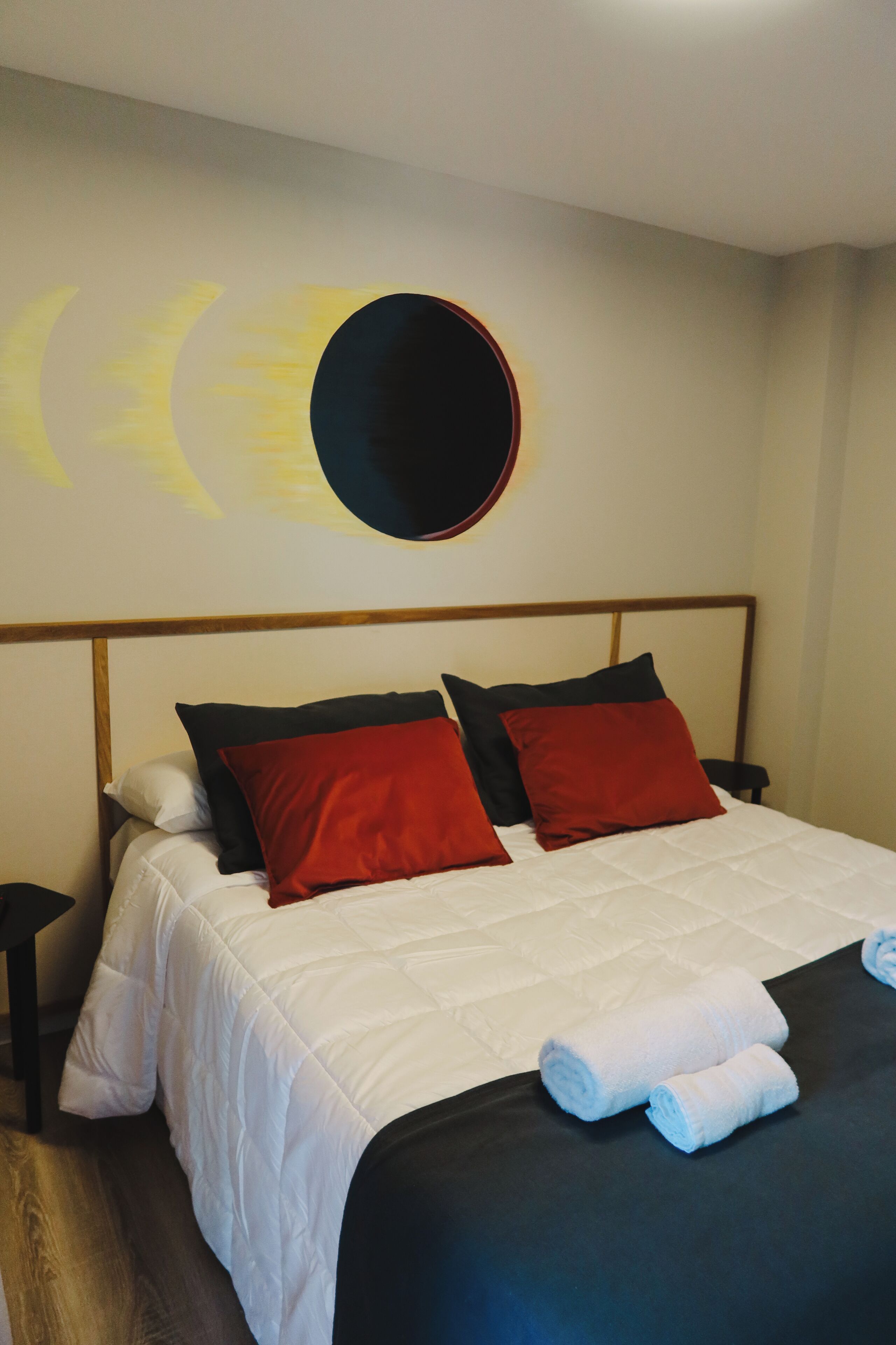 A neatly made bed with white and red bedding, a round mirror on the wall, and a wooden headboard.