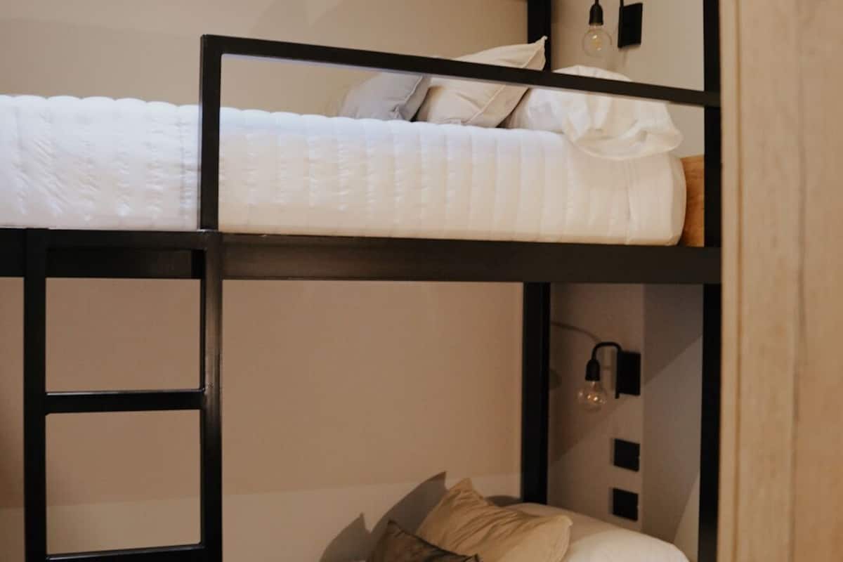 A bunk bed with a ladder, a bedside table, and a wall-mounted light fixture.