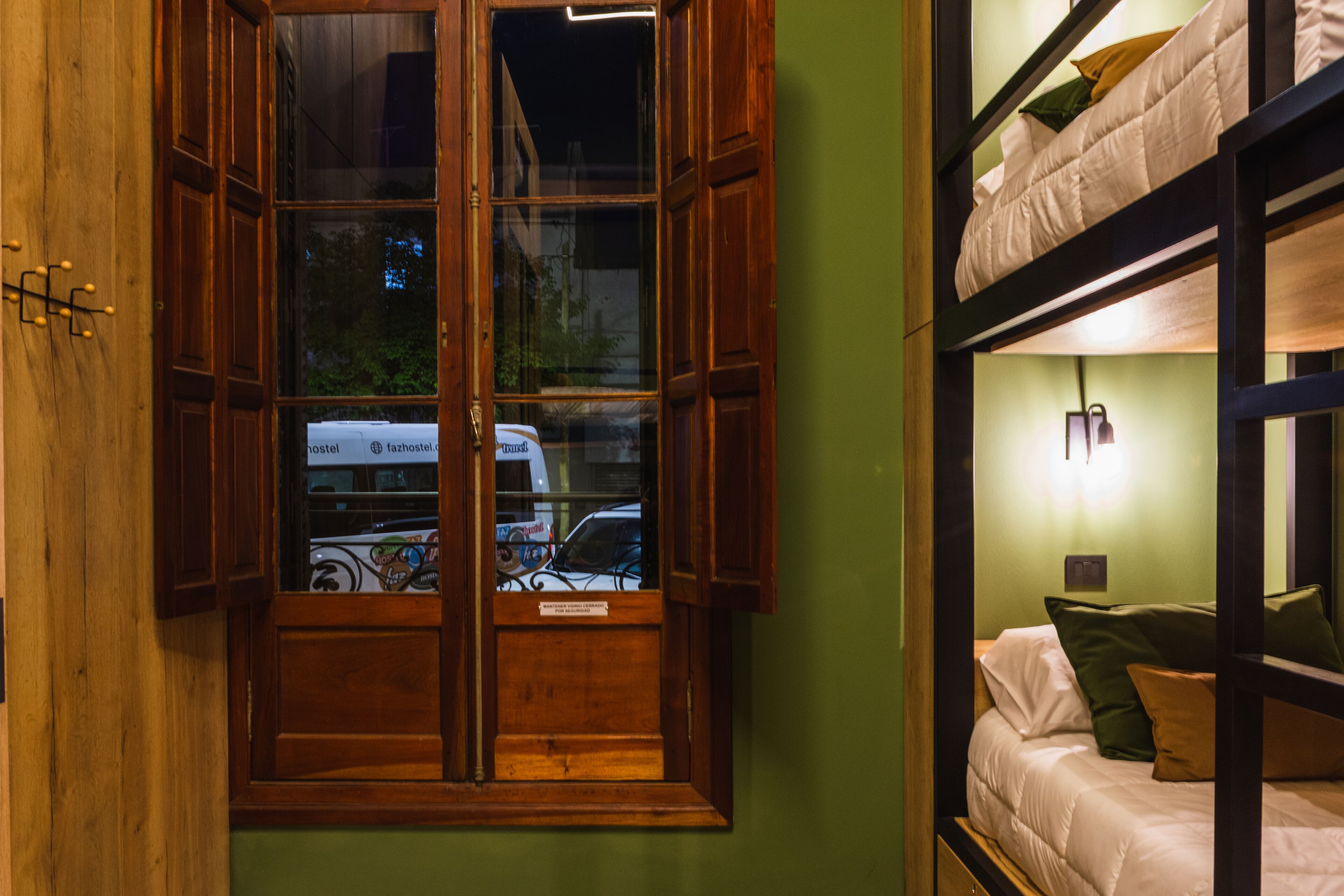Una habitación con literas, un armario de madera y una ventana que da a una calle y coches estacionados.