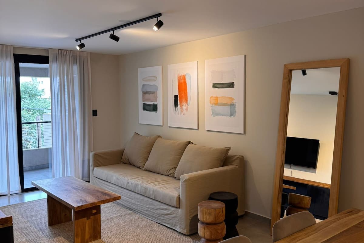 A modern living room with a sofa, coffee table, and chairs. There are abstract paintings on the wall and a large mirror.