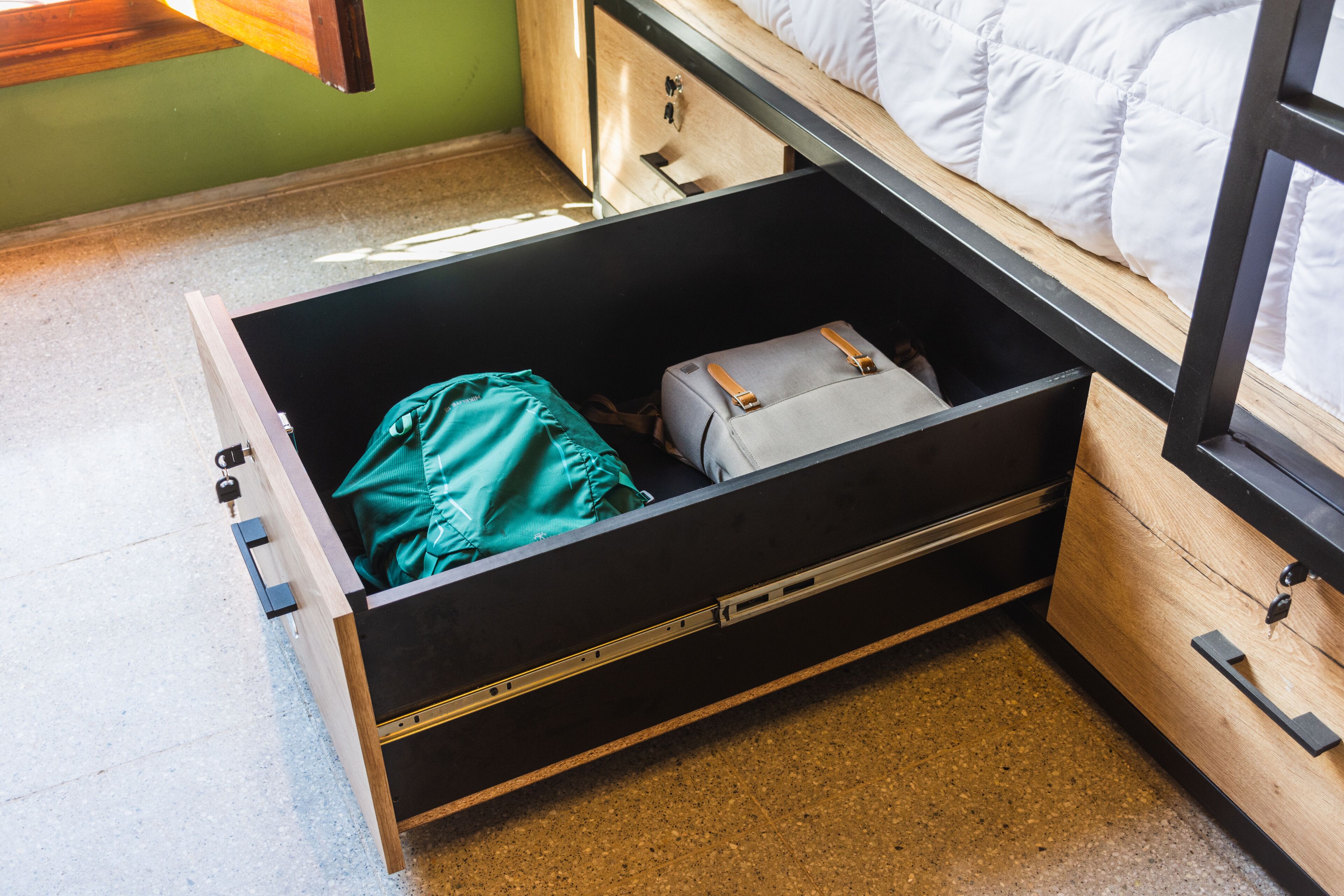 A compact room with a bed, a drawer with a suitcase, and a window.