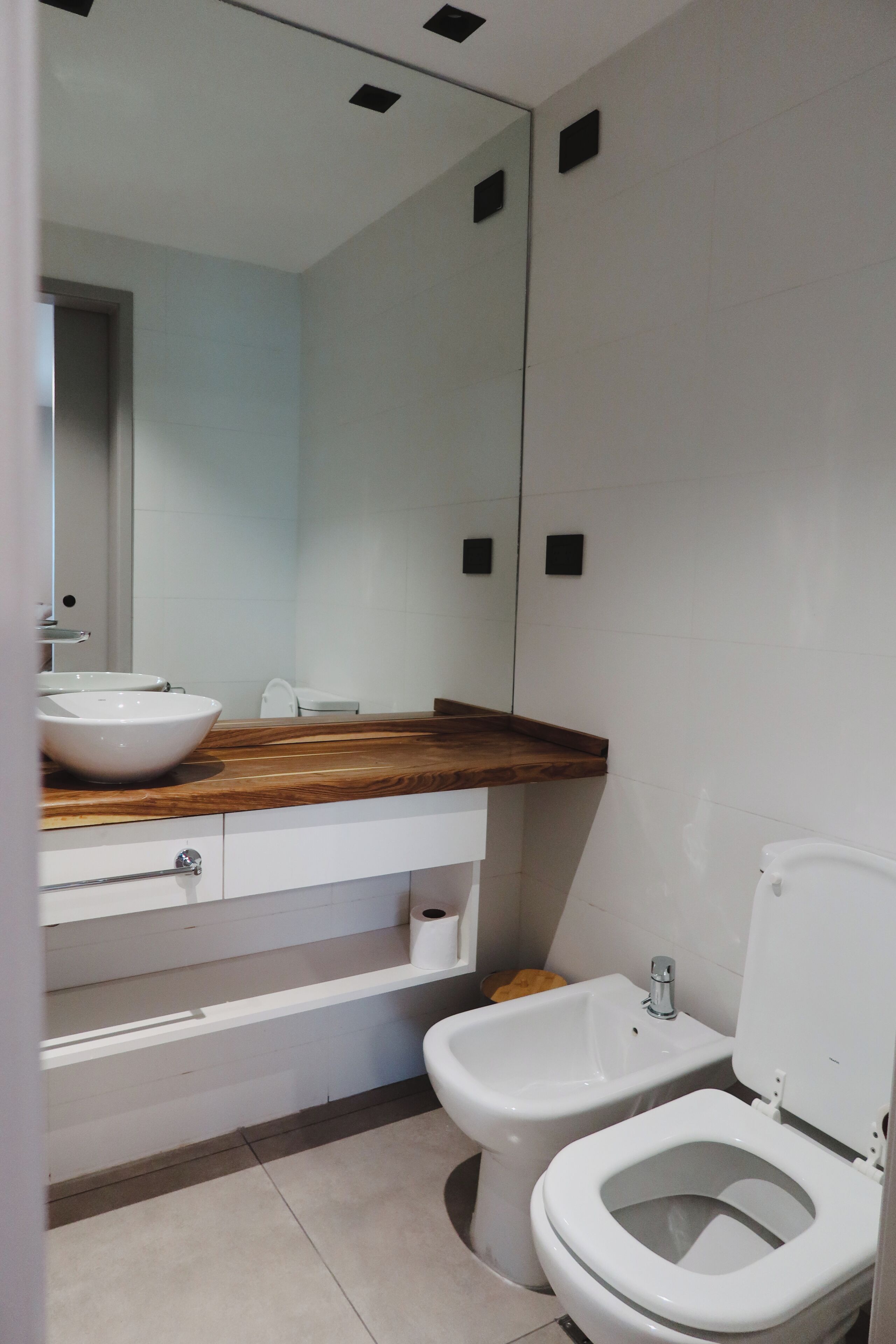 A modern bathroom with a wooden vanity, a white sink, a bidet, and a toilet.
