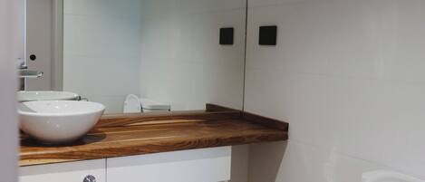 Un baño moderno con un mueble de tocador de madera, un lavabo blanco, un bidé y un inodoro.