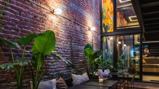 A cozy indoor seating area with brick walls, large green plants, and modern furniture. - FAZ HOSTEL BOUTIQUE (Córdoba)