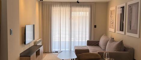 A modern living room with a dining area, featuring a sofa, a TV, and a dining table with chairs.
