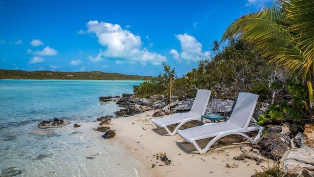 A beach with clear turquoise water, white lounge chairs, and rocky terrain. - Chalk Sound Waterfront Cottage: Pool & Kayak (Providenciales)