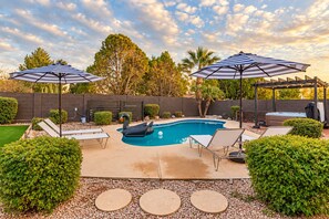 A backyard with a swimming pool, lounge chairs, and umbrellas.