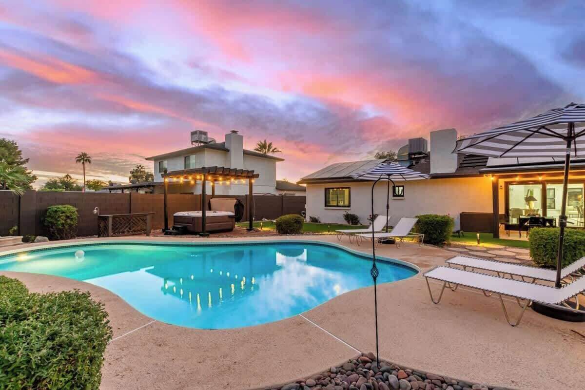 A backyard with a swimming pool, lounge chairs, and a pergola with string lights.